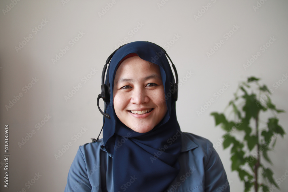 Beautiful Asian muslim woman using headphones speaking to camera, explaining something. Professional teacher mentor customer service support doing online chat or video call Beautiful Asian muslim woman using headphones speaking to camera, explaining something. Professional teacher mentor customer service support doing online chat or video call