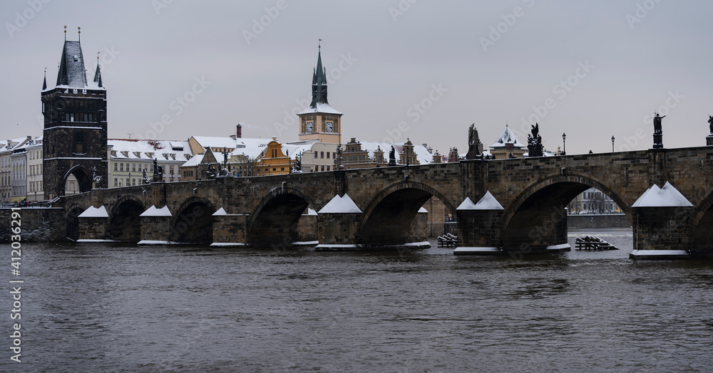 Fototapeta premium panoramic view of the snow-covered Charles Bridge on the Vltava River and snow on the roofs of buildings and towers in the center of the old town of Prague