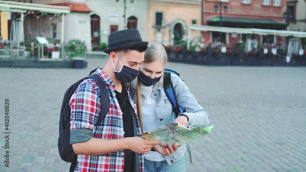 Two tourists in protective masks checking map on central city square, then admiring some beautiful place. Travel during the pandemic.
