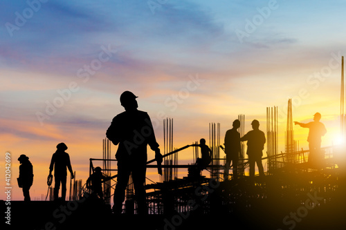 Silhouette of Engineer and worker on building site, construction site at sunset in evening time.