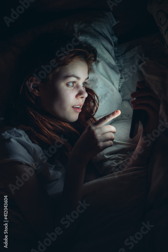 woman with a phone in her hands lies in bed at night before going to bed technology