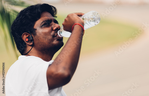 Close up Asian young sport runner black man wear athlete headphones he drinking water from a bottle after running at the outdoor street health park, healthy exercise workout concept