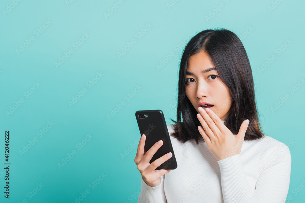 Portrait female anxious scared on the phone seeing bad news, Young beautiful Asian woman surprised shocked with mobile phone close mouth with palm, studio shot isolated on a blue background Portrait female anxious scared on the phone seeing bad news, Young beautiful Asian woman surprised shocked with mobile phone close mouth with palm, studio shot isolated on a blue background