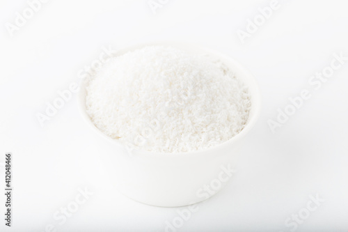 Fresh coconut flakes in white bowl isolated on white background.
