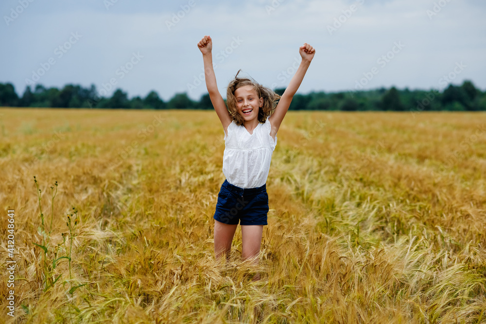 A happy and smiling girl jumps with her arms outstretched in a wheat field A happy and smiling girl jumps with her arms outstretched in a wheat field