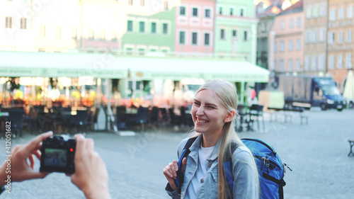 Medium shot of man making photos of female tourist on the view of city market square. Blonde woman making faces and smiling.