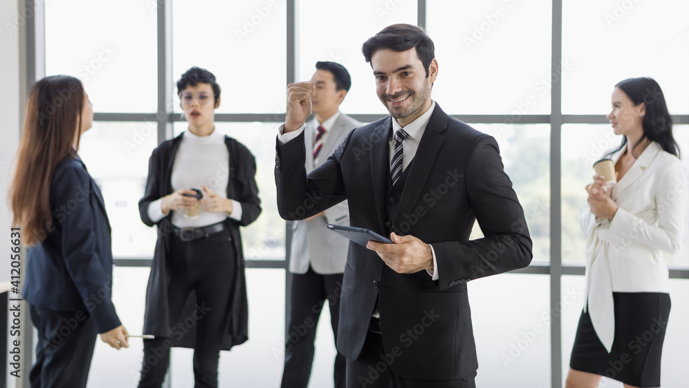 businessman in black suit holding tablet computer and rise his punch in front of group of diversity businesspeople. businessman in black suit holding tablet computer and rise his punch in front of group of diversity businesspeople.