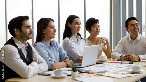 Group of five diversity businessmen, two men and three women sitting at meeting desk and pay attention for speaker of the conference.