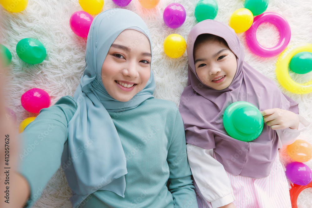 A beautiful mother and lovely daughter, Asian Muslim family, lay down on floor with colorful toys around them and taking selfie photo together. A beautiful mother and lovely daughter, Asian Muslim family, lay down on floor with colorful toys around them and taking selfie photo together.