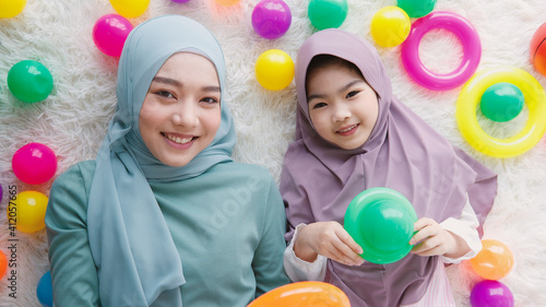A beautiful mother and lovely daughter, Asian Muslim family, lay down on floor with colorful toys around them and looking to the camera. Top view angle shot