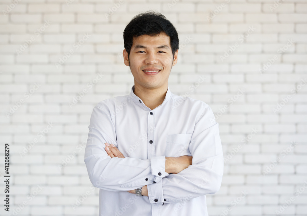 Portrait of a happy Asian young businessman on white brick wall background cross his arms and looking at camera with a warm smile. Close up face of happy successful business man Portrait of a happy Asian young businessman on white brick wall background cross his arms and looking at camera with a warm smile. Close up face of happy successful business man