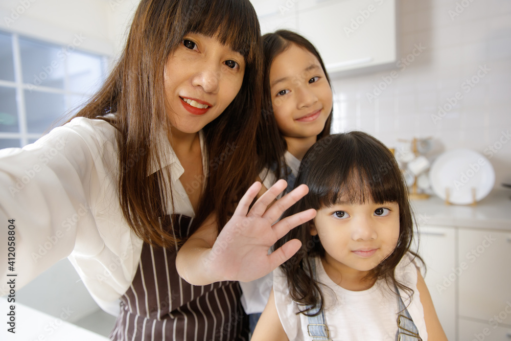 Cute and beautiful mother with two young and little daughters, 3 years and 7 years old, taking a selfie photo with a smartphone in modern kitchen. Concept love and relationship of family Cute and beautiful mother with two young and little daughters, 3 years and 7 years old, taking a selfie photo with a smartphone in modern kitchen. Concept love and relationship of family