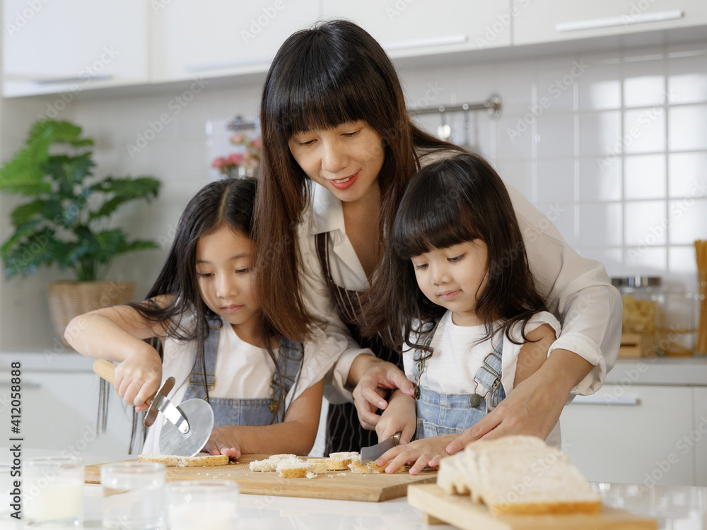 Beautiful and cute Asian mother teaching and showing the 2 daughters, 3 years and 7 years old, how to cut and slice bread