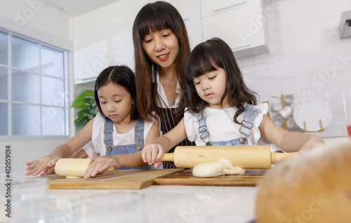 A cute Asian mother teaching the two little daughters, 3 years and 7 years old, how to mak bread and bakery in modern kitchen. Idea for love and relationship in family