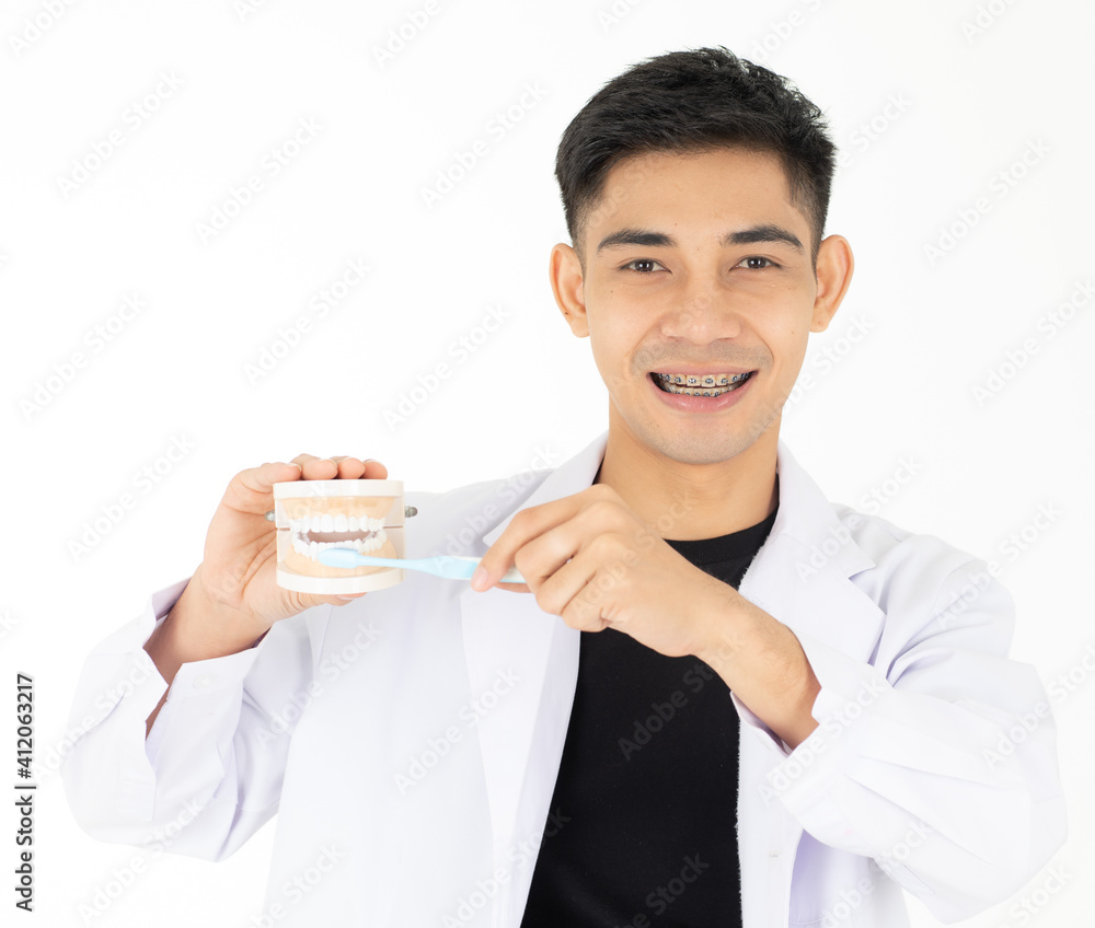 A young and handsome Asian teen man smiling with steel brach holding and showing the model of a good tooth human mouth and how to brush. Isolated on white background A young and handsome Asian teen man smiling with steel brach holding and showing the model of a good tooth human mouth and how to brush. Isolated on white background