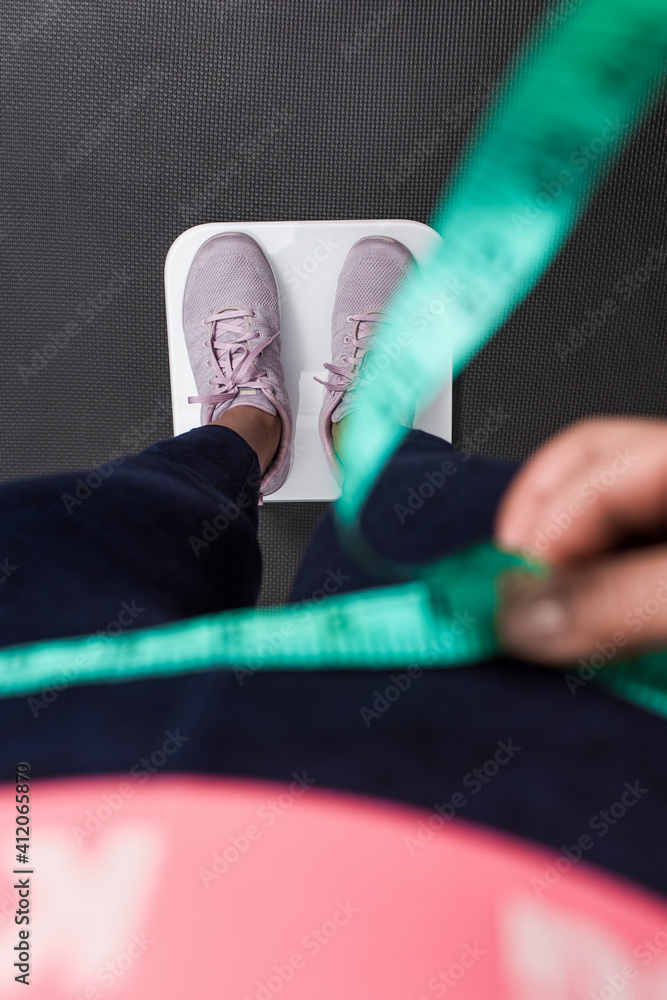 Vertical photography close up woman measuring waist, focus on the sneakers at the white scale.