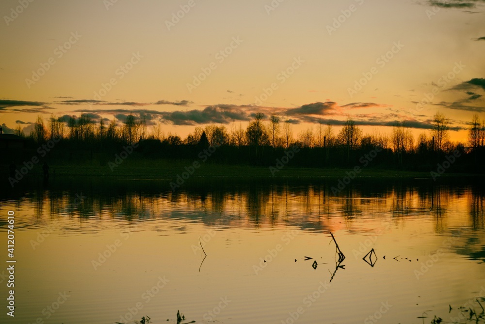 Spring landscape with dramatic after-sunset sky reflected in the water, silhouettes of trees on the shore. Evening calm on the river. Bright afterglow.
