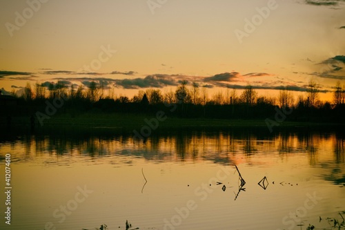 Spring landscape with dramatic after-sunset sky reflected in the water  silhouettes of trees on the shore. Evening calm on the river. Bright afterglow.