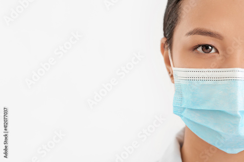 Portrait of female Asian doctor in medical mask on light background