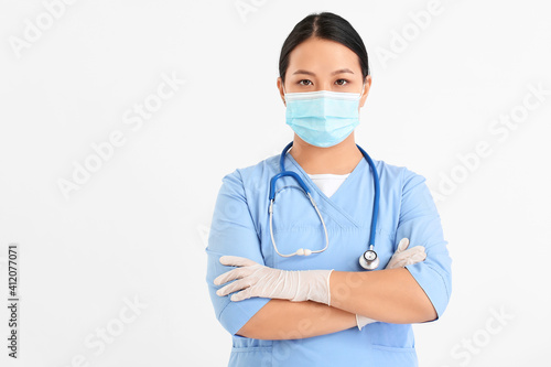 Portrait of female Asian doctor in medical mask on light background