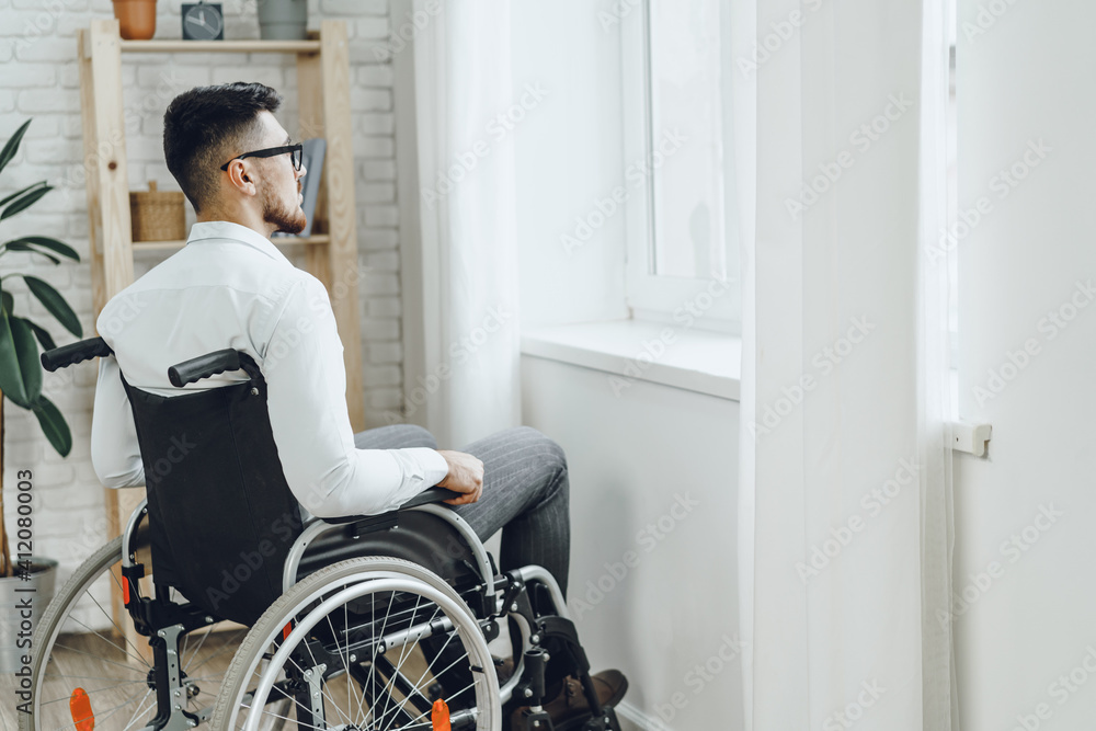 Young disabled man sitting in a wheelchair near the window Young disabled man sitting in a wheelchair near the window