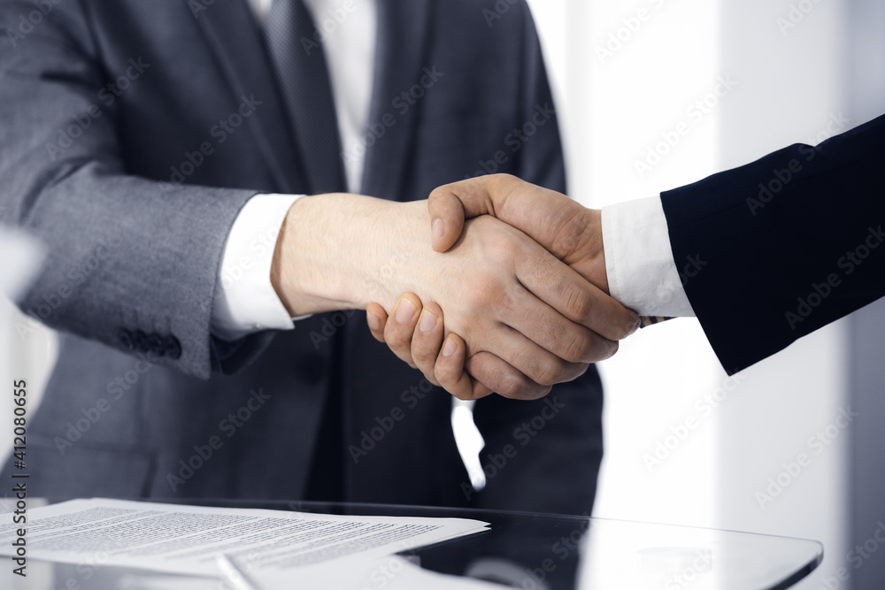 Unknown diverse business people are shaking hands finishing contract signing, close-up. Business and handshake concept