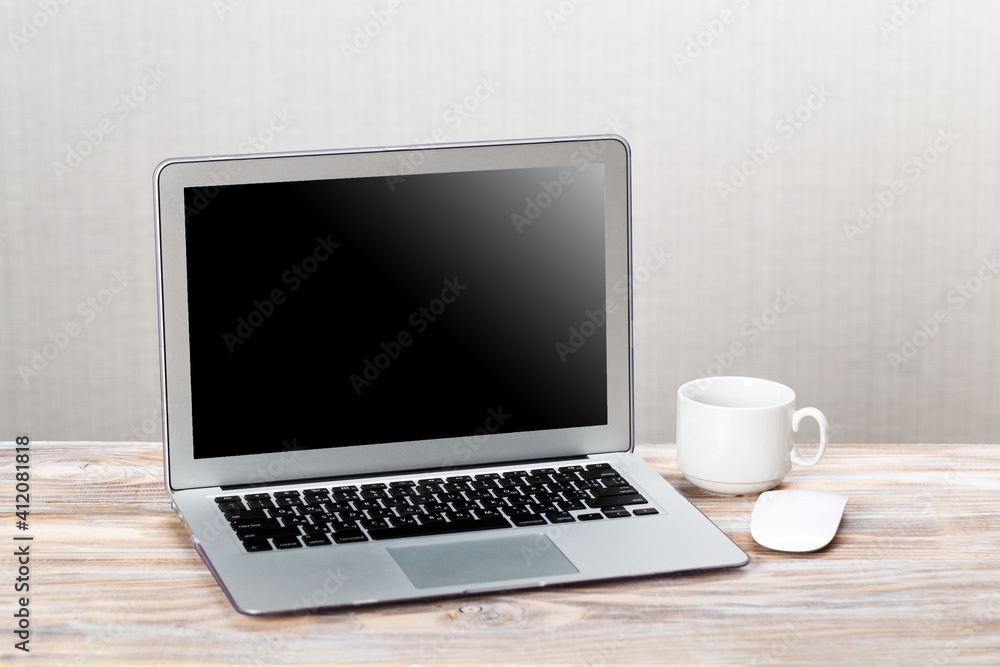 Laptop with blank screen for product display and cup of coffee on wooden table