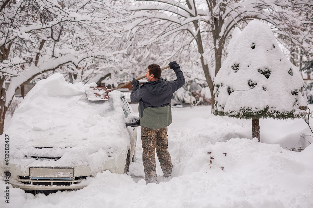 A man cleans the car from snow in winter.