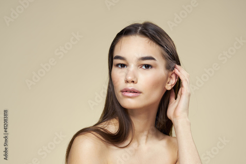 Brunette with bare shoulders close-up long hair beige background clean skin