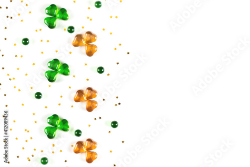 Shamrock symbols made of green and orange glass hearts lying on white background with sparse gold stars confetti. Happy St. Patrick's Day Irish holiday card 17 march lucky clover. Flat lay, copy space