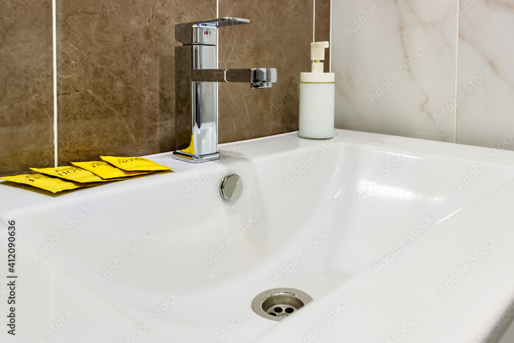 Fototapeta premium White ceramic sink with liquid soap bottle and packets with disposable shampoo