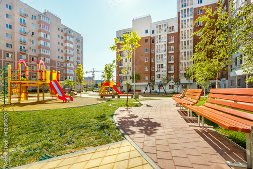 New modern green courtyard of city high-rise buildings with children playground, walkways and benches in sunny summer day
