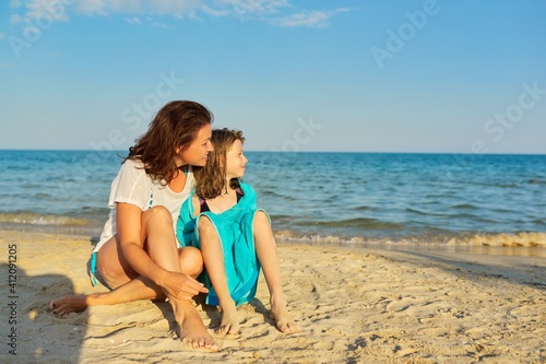 Mature mom and preteen daughter hugged on a sandy beach