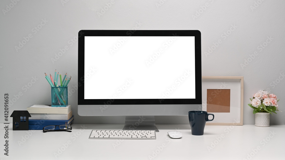 Front view of modern computer with blank screen and office supplies on white office desk. Front view of modern computer with blank screen and office supplies on white office desk.