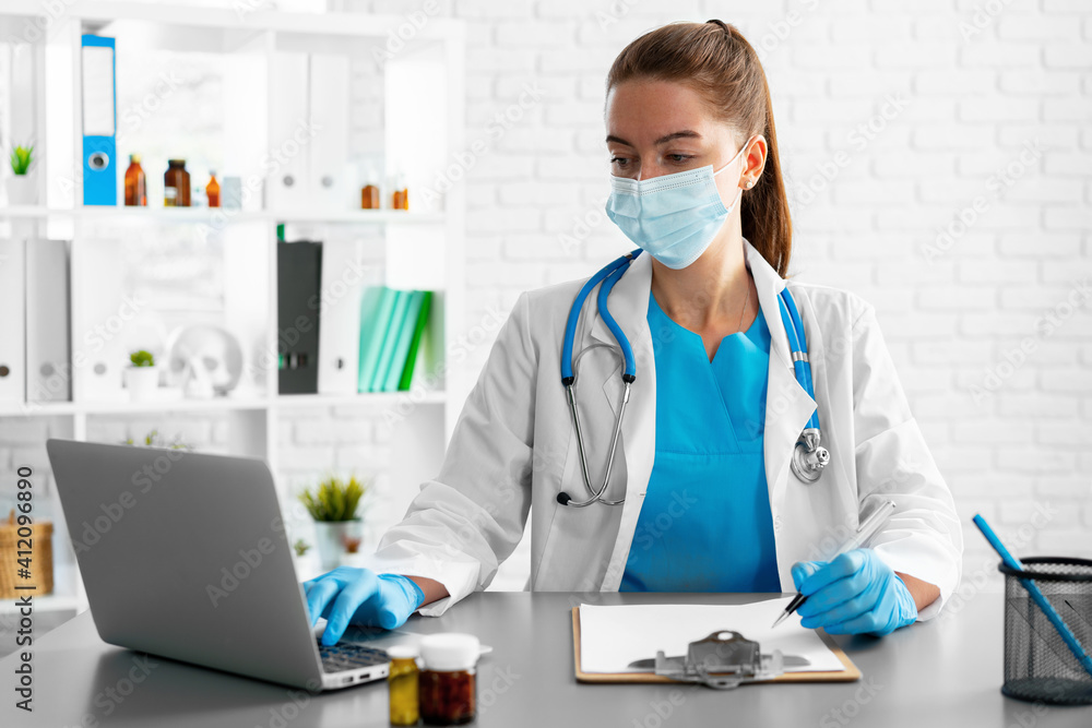 Young woman doctor sitting at working table using laptop Young woman doctor sitting at working table using laptop