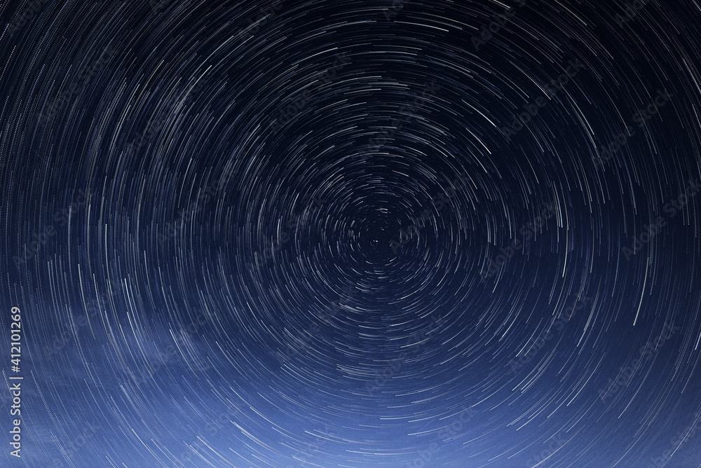 Stellar trails, the rotation of bright stars at night around the Polar Star against a blue sky
