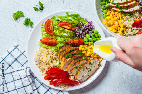 Grilled chicken breast with brown rice and vegetables in white plate, gray background, top view. Healthy food concept.