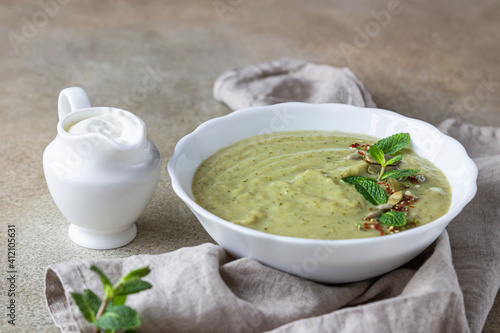Vegetarian cream soup of green vegetables (broccoli, green peas, spinach) served with mint and seeds on concrete background. Clean eating, healthy food concept.