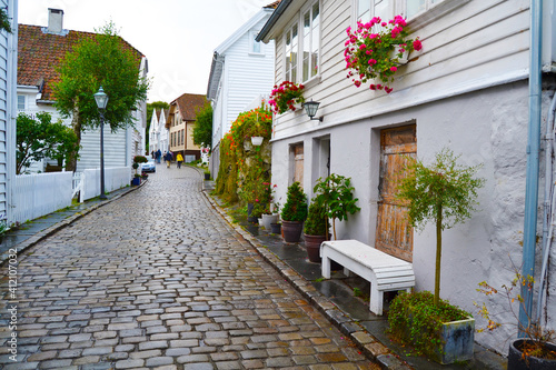 White wooden houses decorated with flowers and plants in the historic district Gamle Stavanger (Old Stavanger), Norway. Rainy day in summer season in Stavanger.