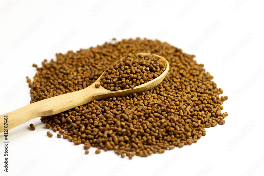 Buckwheat tea in a wooden spoon on a white background. Isolate. Buckwheat tea close-up macro photography. Scattered buckwheat tea pellets on white background. Buckwheat tea in a wooden spoon on a white background. Isolate. Buckwheat tea close-up macro photography. Scattered buckwheat tea pellets on white background.