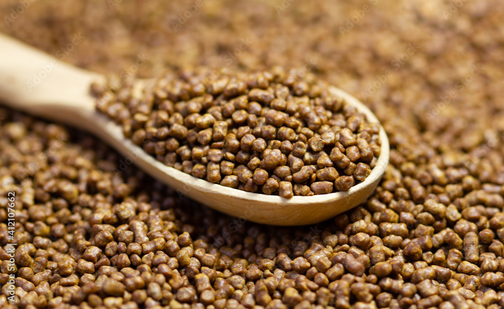 Buckwheat tea in a wooden spoon. Buckwheat tea close-up macro photography. Scattered buckwheat tea pellets brown background. Buckwheat tea in a wooden spoon. Buckwheat tea close-up macro photography. Scattered buckwheat tea pellets brown background.