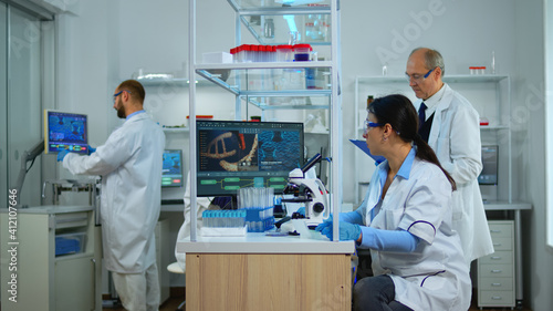 Team of doctors innovating vaccine against coronavirus in modern equipped laboratory looking at samples under microscope. Multiethnic team examining treatment evolution using high tech for research.