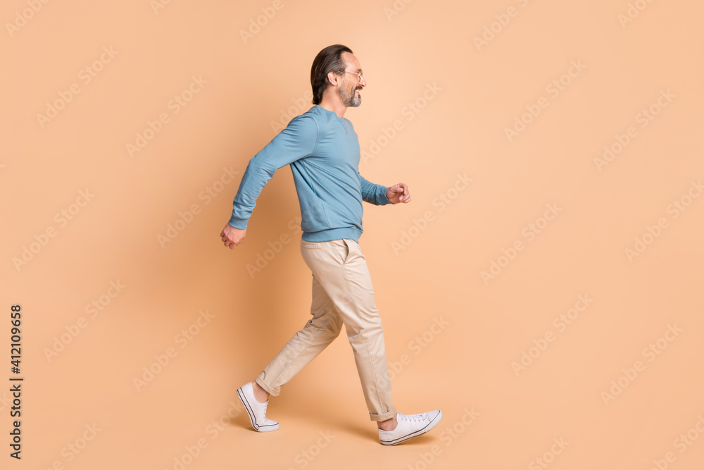Full length profile photo of guy walk wear eyewear blue pullover pants sneakers isolated beige color background
