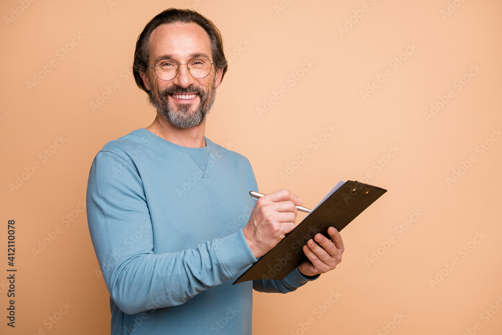 Photo portrait of man writing notes on clipboard isolated on pastel beige colored background Photo portrait of man writing notes on clipboard isolated on pastel beige colored background