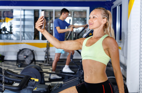 Positive smiling glad sporty girl taking selfie during workout at gym