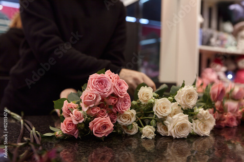 Florist works with colors. Flower seller chooses flowers for future bouquet. Flowers shop worker in a mask standing in flower shop and checking flowers in glass vase.