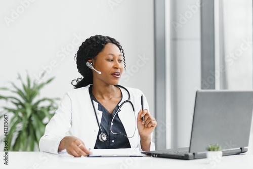 African American woman doctor working at her office online using portable inormation device. Telemedicine services. Primary care consultations, psychotherapy, emergency services. photo