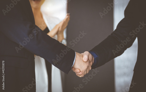 Unknown businesspeople are shaking their hands after signing a contract, while standing together in a sunny modern office, close-up. Business communication, handshake, and marketing concept © cameravit