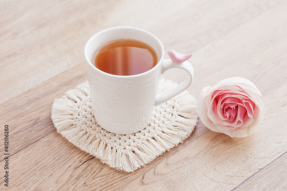 Macrame handmade Hobby. Tea in a cup on white macrame coaster on wooden table with rose. Food stylist. Eco macrame home decoration. St. Valentine's Day Macrame handmade Hobby. Tea in a cup on white macrame coaster on wooden table with rose. Food stylist. Eco macrame home decoration. St. Valentine's Day