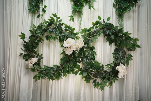 Green leaves and white flowers wreath hanging on white curtains 